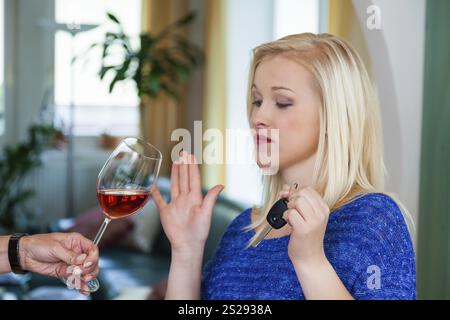 Una giovane donna con le chiavi della macchina rifiuta un bicchiere di vino. Non bere e guidare Foto Stock