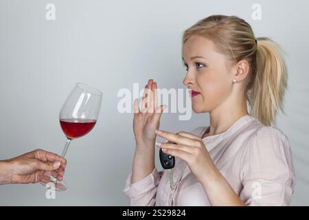 Una giovane donna con le chiavi della macchina rifiuta un bicchiere di vino. Non bere e guidare Foto Stock