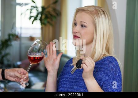 Una giovane donna con le chiavi della macchina rifiuta un bicchiere di vino. Non bere e guidare Foto Stock