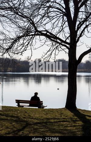 Un solo uomo siede su una panchina di un parco vicino a un lago in Austria Foto Stock