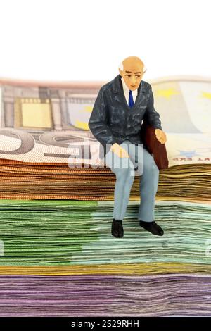 Foto simbolica per la pensione e la sicurezza vecchiaia, figura di un vecchio seduto su una pila di banconote Foto Stock