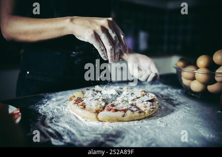 Le mani dello chef versano farina in polvere sull'impasto crudo. Concetto di cucina. Foto Stock