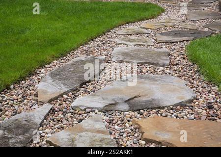 Primo piano di un sentiero in pietra e ghiaia attraverso un prato curato in erba verde in giardino residenziale in estate. Foto Stock