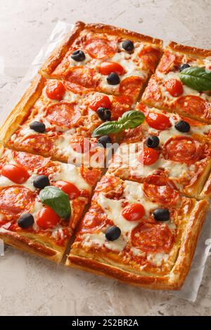 Pasta sfoglia con salsiccia al peperoni, olive, pomodori e mozzarella primo piano su pergamena sul tavolo. Verticale Foto Stock