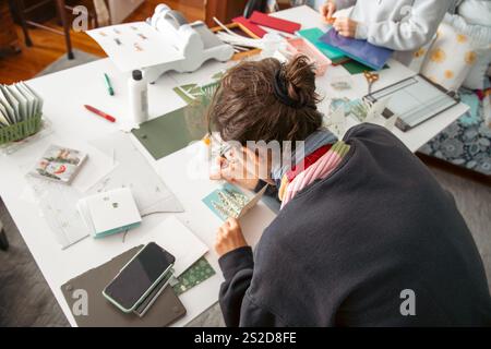 Vista dall'alto posteriore ravvicinata di una donna seduta a un tavolo che prepara carte fatte in casa in uno studio Foto Stock