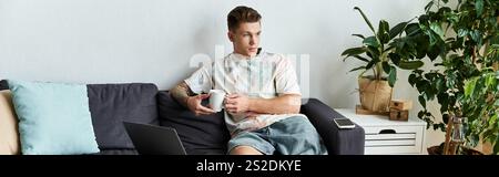 Bel giovane uomo seduto comodamente su un divano, godendosi il suo caffè. Foto Stock