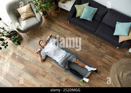Un giovane con una gamba protesica lavora a casa, concentrandosi sull'allenamento con i pesi. Foto Stock