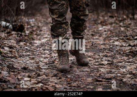 Un soldato in uniforme che cammina lungo un sentiero nella foresta, catturato dalle gambe alla vita Foto Stock