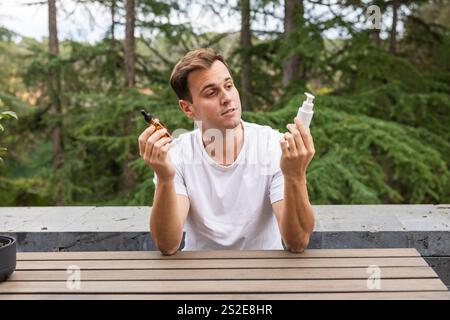 Uomo che sceglie tra due prodotti cosmetici per la sua routine per la cura della pelle all'aperto, Young man confronta Foto Stock