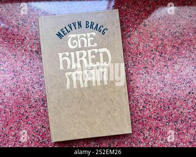Kiev, Ucraina - 07 gennaio 2025: Un libro in copertina rigida intitolato "The hire Man" di Melvyn Bragg, visualizzato su una superficie rossa testurizzata. Foto Stock