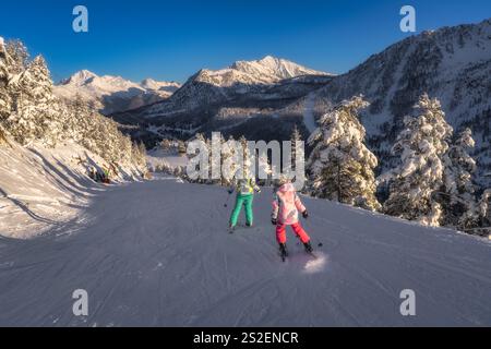 Due sciatori avventurosi scivolano elegantemente lungo i pittoreschi pendii innevati, circondati da montagne maestose e alberi ghiacciati e splendidamente ornati, Mon Foto Stock