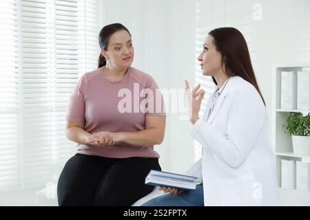 Nutrizionista con notebook che fornisce consigli alle donne in sovrappeso in ospedale Foto Stock