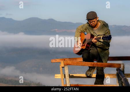 Un turista maschile suona una chitarra al mattino su una cima di una montagna Foto Stock