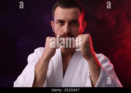 Combattente di karate con luci colorate e fumo su sfondo nero Foto Stock