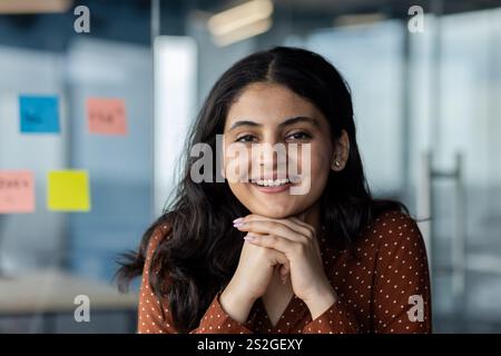 Ritratto ravvicinato di una giovane donna d'affari di successo, lavoratrice d'ufficio che sorride e guarda la fotocamera, lavora all'interno di un ufficio moderno, donna soddisfatta. Foto Stock