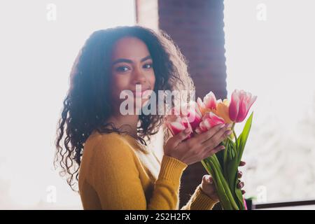 Giovane donna con capelli ricci che tiene i tulipani rosa in luce naturale a casa Foto Stock