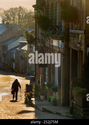 Main Street di Haworth, vista in una soleggiata giornata invernale con una figura sagomata in lontananza. West Yorkshire, Regno Unito. Foto Stock