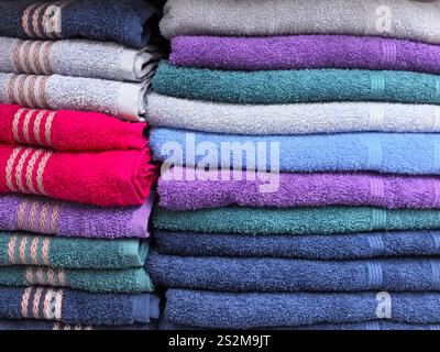 Lussuosi asciugamani in varie tonalità sono impilati in modo ordinato, mostrando le loro ricche texture e colori. L'accordo porta un senso di ordine e calore Foto Stock