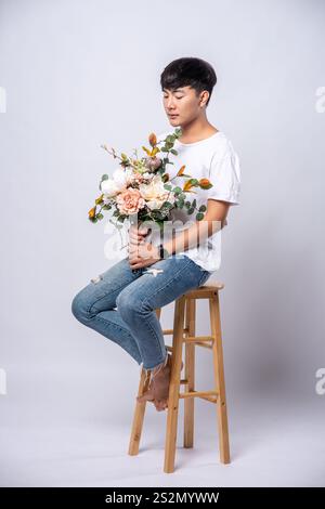 Un giovane con una t-shirt bianca si siede su un seggiolone e tiene i fiori. Foto Stock