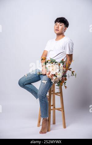 Un giovane con una t-shirt bianca si siede su un seggiolone e tiene i fiori. Foto Stock