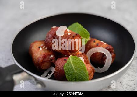 Salsiccia avvolta nella pancetta di maiale in una padella con sesamo e menta. Messa a fuoco selettiva. Foto Stock