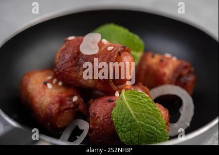 Salsiccia avvolta nella pancetta di maiale in una padella con sesamo e menta. Messa a fuoco selettiva. Foto Stock