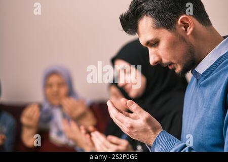 Famiglia musulmana che fa rompere iftar dua il digiuno durante il Ramadan tavolo da pranzo a casa insieme pregando con le mani in alto. Foto Stock