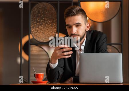 Ritratto di un giovane uomo d'affari felice seduto alla sua scrivania in ufficio e che usa un telefono. Foto Stock