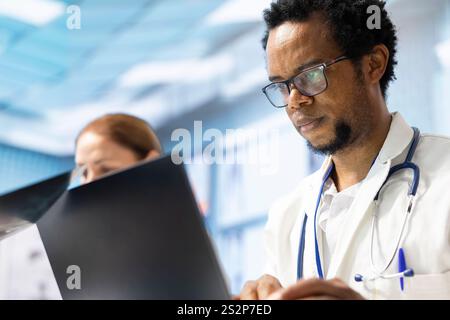Diversi team di medici che esaminano i risultati dei raggi X e i dati sanitari in una riunione di gabinetto, consultando i colleghi prima di effettuare una diagnosi. Medici che lavorano insieme per la guarigione sanitaria. Foto Stock
