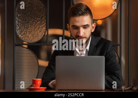 Un giovane uomo d'affari felice che utilizza un notebook mentre lavora in ufficio. Foto Stock