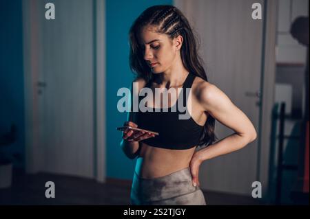 Giovane donna attraente che utilizza uno smartphone mentre indossa abiti fitness a casa Foto Stock