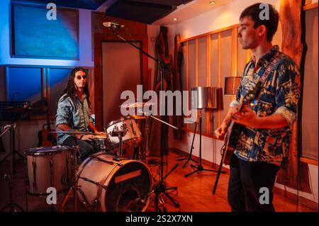 Batterista che ascolta il chitarrista jamming prima della sessione di registrazione. Sono concentrati nel processo. Varie apparecchiature musicali all'interno della cornice. Una band Foto Stock