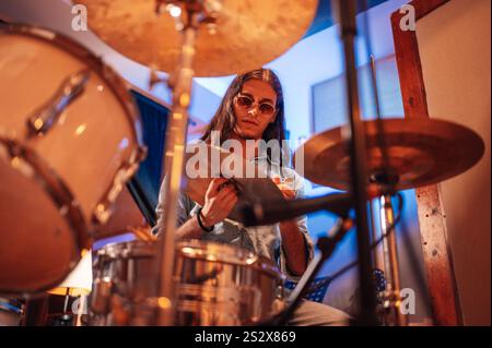 Ritratto di un musicista con capelli lunghi che registra un nuovo album in studio con il loro produttore e ingegnere del suono. Concentrati sulla faccia di un batterista mentre holdin Foto Stock