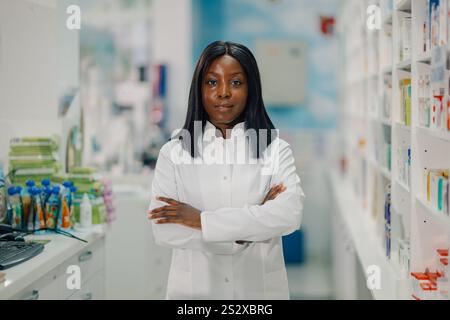 Farmacista sicuro in una farmacia ben fornita, sorridendo felicemente con un camice da laboratorio bianco Foto Stock