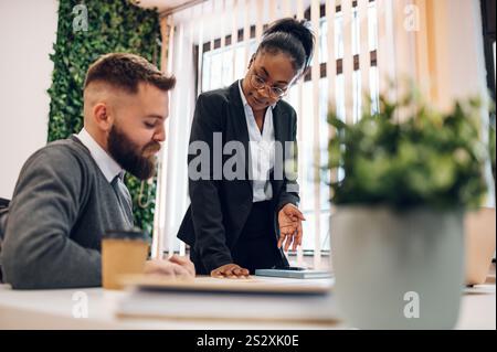 Team leader che analizza le statistiche dei dati di vendita o spiega la strategia di marketing a diversi colleghi multirazziali alla riunione di brainstorming. Autobus Foto Stock