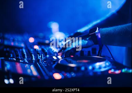 Primo piano del dj che fa musica con le mani sulla console di mixaggio in un festival di musica elettronica di sera. Immagine ritagliata delle mani con console di mixaggio che crea musica Foto Stock