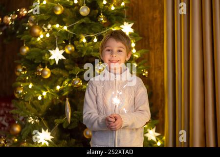 Bambino della scuola, ragazzo, in piedi a casa a natale, tenendo sparkler davanti all'albero di Natale, Natale Foto Stock