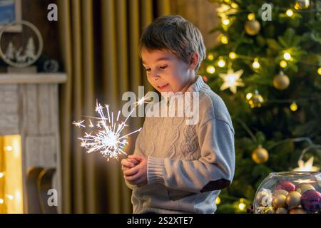 Bambino della scuola, ragazzo, in piedi a casa a natale, tenendo sparkler davanti all'albero di Natale, Natale Foto Stock