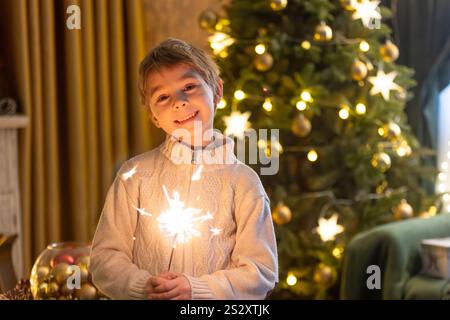 Bambino della scuola, ragazzo, in piedi a casa a natale, tenendo sparkler davanti all'albero di Natale, Natale Foto Stock