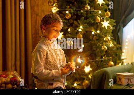 Bambino della scuola, ragazzo, in piedi a casa a natale, tenendo sparkler davanti all'albero di Natale, Natale Foto Stock