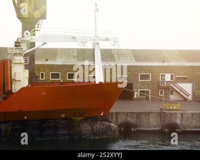 Scena portuale ndustriale con una nave dallo scafo rosso attraccata a Walvis Bay, Namibia, con attrezzature per il trasporto merci ed edifici portuali visibili. Foto Stock