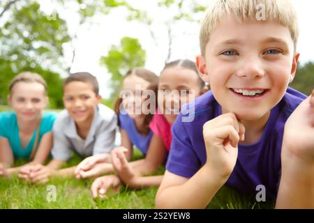 Amici, felici e bambini nel parco per il legame, l'infanzia e il divertimento sul campo d'erba. Amicizia, vita all'aperto e ritratto di bambini diversi per Foto Stock
