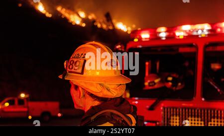 Malibu, California, Stati Uniti 7 gennaio 2025. Un Vigili del fuoco di LA County in un cappello da 89 è acceso rosso e giallo dalle luci dei veicoli di emergenza. Un incendio scoppiò il 7 gennaio 2025, come si vede dalla PCH (Pacific Coast Highway) nella ricca città di Pacific Palisades, ai margini di Malibu, CA, a causa di venti di Santa Ana insolitamente forti che superavano i 100 MPH (Credit Image: © Amy Katz/ZUMA Press Wire) SOLO PER L'USO EDITORIALE! Non per USO commerciale! Foto Stock