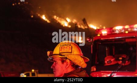Malibu, California, Stati Uniti 7 gennaio 2025. Un Vigili del fuoco di LA County in un cappello da 89 è acceso rosso e giallo dalle luci dei veicoli di emergenza. Un incendio scoppiò il 7 gennaio 2025, come si vede dalla PCH (Pacific Coast Highway) nella ricca città di Pacific Palisades, ai margini di Malibu, CA, a causa di venti di Santa Ana insolitamente forti che superavano i 100 MPH (Credit Image: © Amy Katz/ZUMA Press Wire) SOLO PER L'USO EDITORIALE! Non per USO commerciale! Foto Stock
