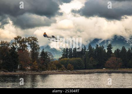 Ein Wasserflugzeug der Harbour Air Seaplanes im Landeanflug vor dem mit Bäumen begrünten Ufer, im Hintergrund Berglandschaft, Vancouver, Kanada. Foto Stock