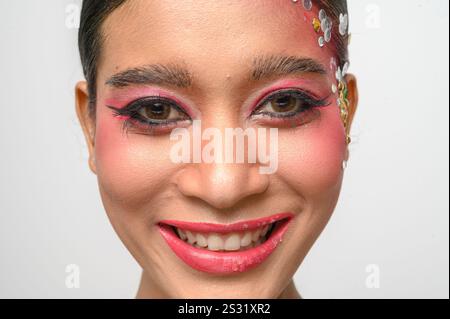 Donna che indossa trucco e decorazioni rosa sul viso. Isolato su sfondo bianco Foto Stock