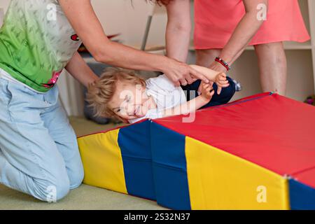 Fisioterapia domestica di un bambino handicappato con paralisi cerebrale. Terapia per bambini con esigenze speciali a casa con la famiglia. Diversità e inclusione. Foto Stock