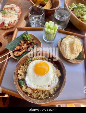 Piatto di cucina tradizionale balinese con Nasi Goreng con uova fritte, spiedini di pollo, verdure fresche e contorni assortiti in ciotole di legno Foto Stock