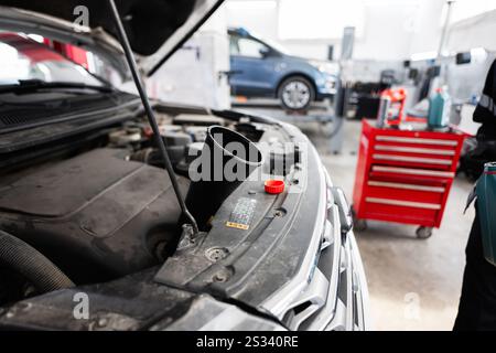Primo piano del motore di un'auto sottoposto a manutenzione ordinaria in un'officina di riparazione auto. Gli attrezzi e le parti della vettura sono visibili sullo sfondo, sottolineando una p Foto Stock