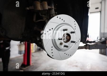 Immagine dettagliata del disco del freno di un'auto, che evidenzia il design industriale e i meccanici di precisione in un'officina di riparazione auto. Foto Stock